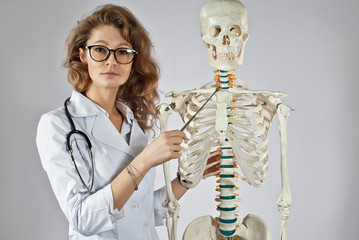 Woman in medical gown. Doctor with skeleton layout. Girl medic in glasses isolated on a white...