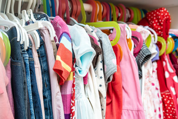 Large selection of bright, children's clothes for a girl hanging in a closet, on hangers.