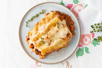 Cannelloni pasta with filling of ground beef, tomatoes, baked with bechamel tomato sauce and mozzarella. Classical Italian cuisine, white tablecloth with embroidery, rustic style, top view