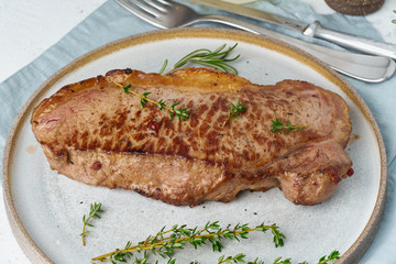 Keto ketogenic diet beef steak, striploin on gray plate on white background. Paleo food recipe with whole big piece of meat and seasoning. Close up, side view