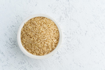 Brown rice in white bowl on white background. Dried cereals in cup, vegan food, fodmap diet. Top view, close up.