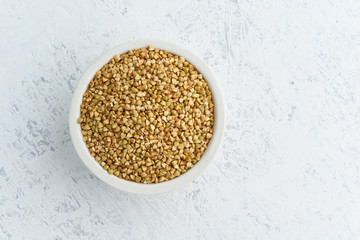 Green buckwheat in white bowl on white background. Dried cereals in cup, vegan food, fodmap diet. Top view, close up.