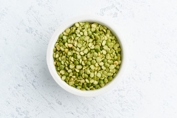 Green peas in white bowl on white background. Dried cereals in cup, vegan food. Top view, close up.