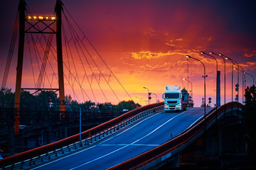 truck with container rides over the bridge, beautiful sunset, freight cars in industrial seaport,...