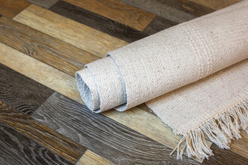 Rolled natural cotton rug on the wooden linoleum background.