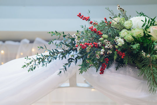 marriage flower composition on arch with chrysanthemum, rose, pistachio, thuja, waxflower, ilex, eustoma, pine branch for winter wedding indoors decoration, close-up stock photo image