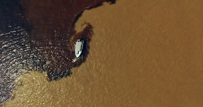 Aerial view over the white boat standing on the border of the confluence between the dark Rio Negro and the pale sandy-colored Amazon River upper flow, referred as the Solim&otilde;es River. Manaus. Brazil
