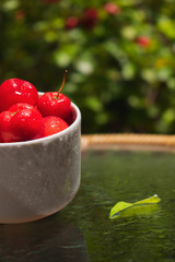 Acerola fruit in a bowl at table on garden, typical Brazilian fruit concept image.