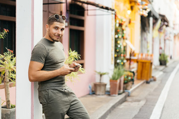 Portrait of a young man in green clothes, outdoors, holding a mobile phone and smiling. Communication in social networks.