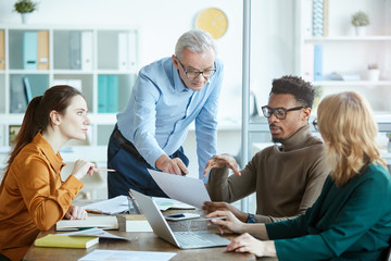 Group of business people pointing at business contract and discussing its details together at the table at meeting at office
