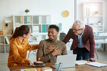 Business people bringing cake with candles for their colleague and they congratulating him with birthday during work day