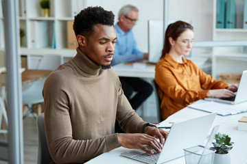 Multiethnic business people sitting on their workplaces and typing on laptop computers at office