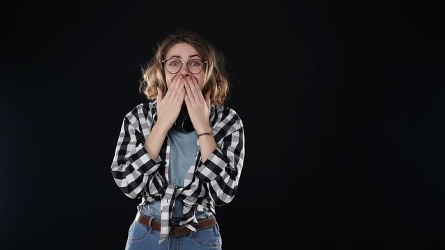 Over excited female with curly hairstyle, laughs happily, expresses sincere emotions, being surprised by good news. Happy young female in plaid shirt and jeans gesturing, super surprised over black