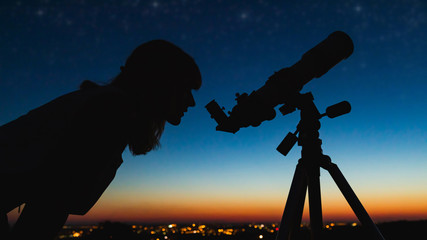 Astronomer with a telescope watching at the stars and Moon with blurred city lights in the...