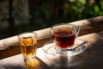 Coffee cup with saucer and glass of hot tea under afternoon window light, green garden background.