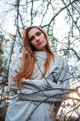 Girl in straitjacket, outside in the woods, branches surrounding her.