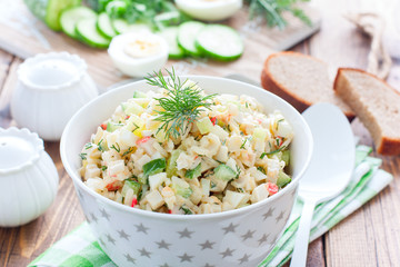 Salad with crab sticks, fresh cucumbers and rice in a white bowl, horizontal