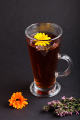 Glass of herbal tea with calendula and hyssop on a black background. Side view, close up.
