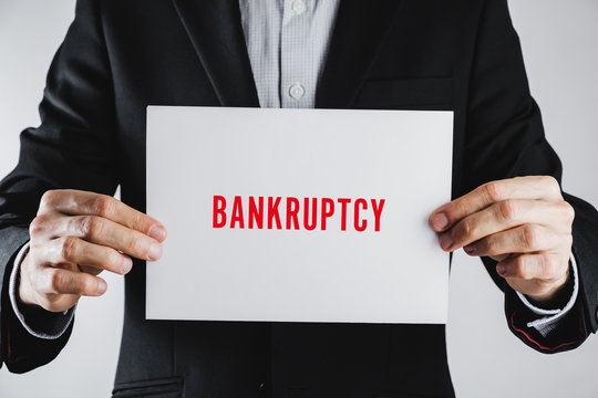 Going bankcrupt, having financial difficulties in business sign. Man in business clothes holds a a paper with word "bankcruptcy"