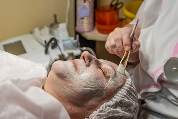 Cosmetic procedure with a cleansing metal mask on the face with nanosilver particles in a beauty salon. It is performed for an age woman. Improving skin turgor, rejuvenation and healing.
