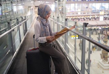 Asian muslim tourist looking on the map to get the direction of destination way when she arrived at Airport. travel and tourism concept.