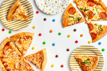 Pieces of pizza and colored sweets on a white background. Birthday with junk food. Children's party. Top view with copy space for text. Flat lay