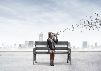 Young woman with megaphone sitting on wooden bench