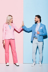 smiling woman and handsome man showing high five on pink and blue background