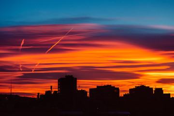 Amazing sunset with orange, pink and red stratus clouds over the city with traces from the planes in the sky. Background for forecast and meteorology concept. Barcelona, Spain.