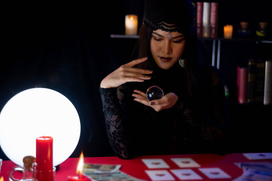 Beautiful young Asian woman Gypsy Fortune teller glowing crystal ball, tarot cards and composition of esoteric astrology object to predict destiny or future.