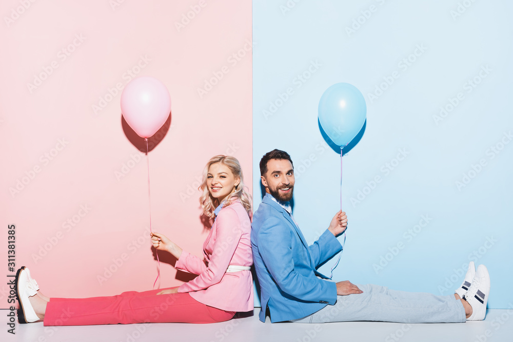 Wall mural back to back view of smiling woman and handsome man holding balloons on pink and blue background