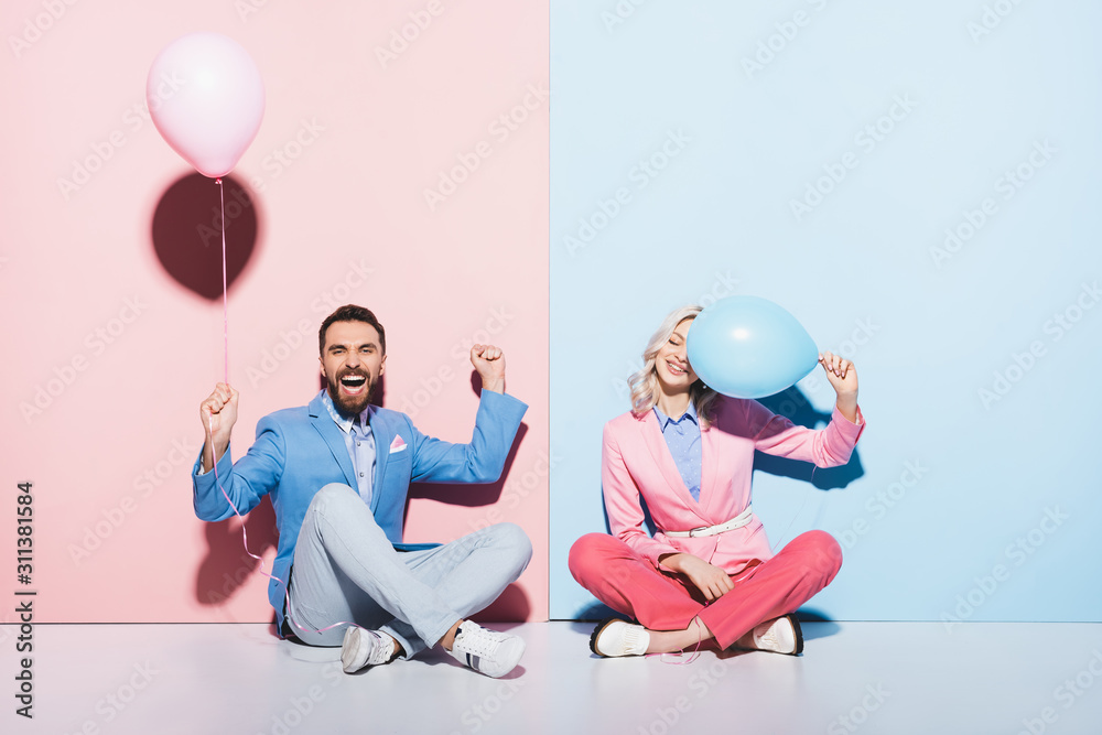 Wall mural attractive woman and handsome man with balloons showing yes gesture on pink and blue background