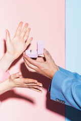 cropped view of man doing marriage proposal to woman on pink and blue background