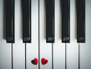 Naklejka premium Two small red hearts on the keyboard of classic piano close-up. Concept of love and romantic music