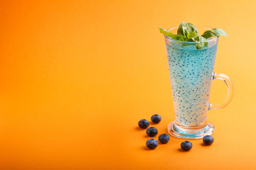 Glass of blueberry blue colored drink with basil seeds on orange background. Morninig, spring, healthy drink concept. Side view
