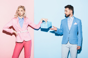 attractive woman holding gift and handsome man pointing with hand on pink and blue background