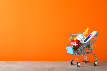 Mini shopping cart with medical supplies on orange background, space for text