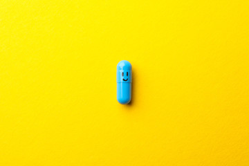 Pill in capsule with happy face on yellow background, space for text - obrazy, fototapety, plakaty