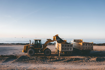 Excavator loads the excavation onto a truck (hydraulic)are heavy construction equipment consisting of an arrow,a bucket and a cabin on a rotating platform.On the beach with the sea and the setting sun