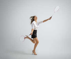 Movement. Woman in office clothes playing badminton with two racket on grey studio background. Businesswoman training in motion, action. Unusual look for sport, new activity. Sport, healthy lifestyle.