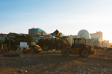 Fototapeta premium Excavator loads the excavation onto a truck (hydraulic)are heavy construction equipment consisting of an arrow,a bucket and a cabin on a rotating platform.On the beach with the sea and the setting sun