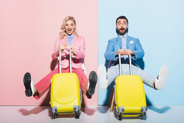 shocked woman and handsome man holding travel bags on pink and blue background