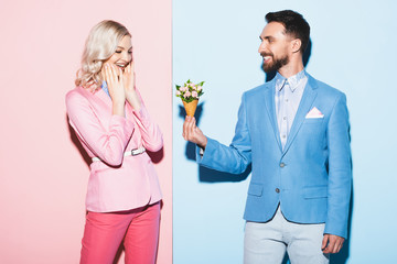 smiling man giving bouquet to shocked woman on pink and blue background