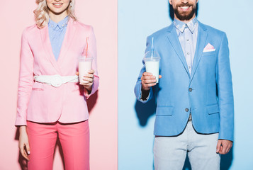 cropped view of smiling woman and man holding cocktails on pink and blue background