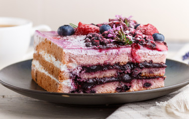 Berry cake with milk cream and blueberry jam on blue ceramic plate with cup of coffee and fresh blueberries on a white wooden background. side view, selective focus.