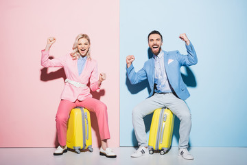 smiling woman and handsome man sitting on travel bags and showing yes gesture on pink and blue background