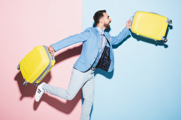 smiling man holding travel bags on pink and blue background