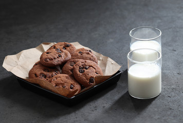 Chocolate chip cookies with dark chocolate slices with milk and coffee on a dark gray background
