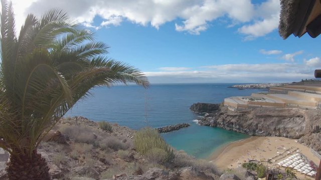 Beautiful hidden tropical beach landscape. 4K footage of headland scene on the coast of Tenerife island. Abama beach. Seascape with turquoise ocean water, palm tree in the foreground and backlight sun