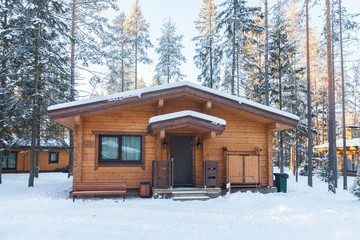 One-storey house made of wooden beams among the trees of the winter forest. Treetops lit by low sun